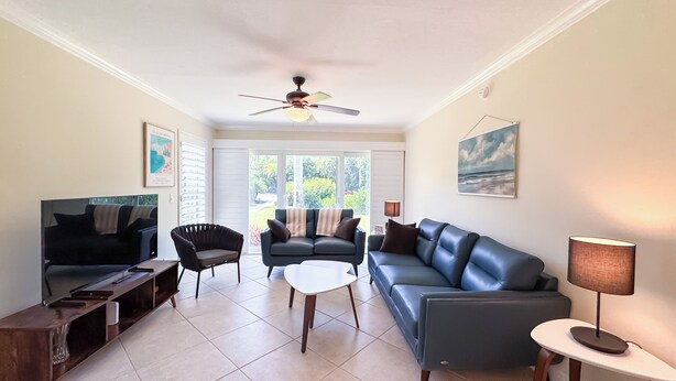 A living room with a ceiling fan, a sofa, a coffee table, and a TV. - Ville De Marco M-1: Beautiful Condo in Olde Marco (Marco Island)
