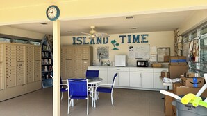 A library with bookshelves, a clock, a table with chairs, and a wall with 'ISLAND TIME' written on it. - Ville De Marco M-1: Beautiful Condo in Olde Marco (Marco Island)