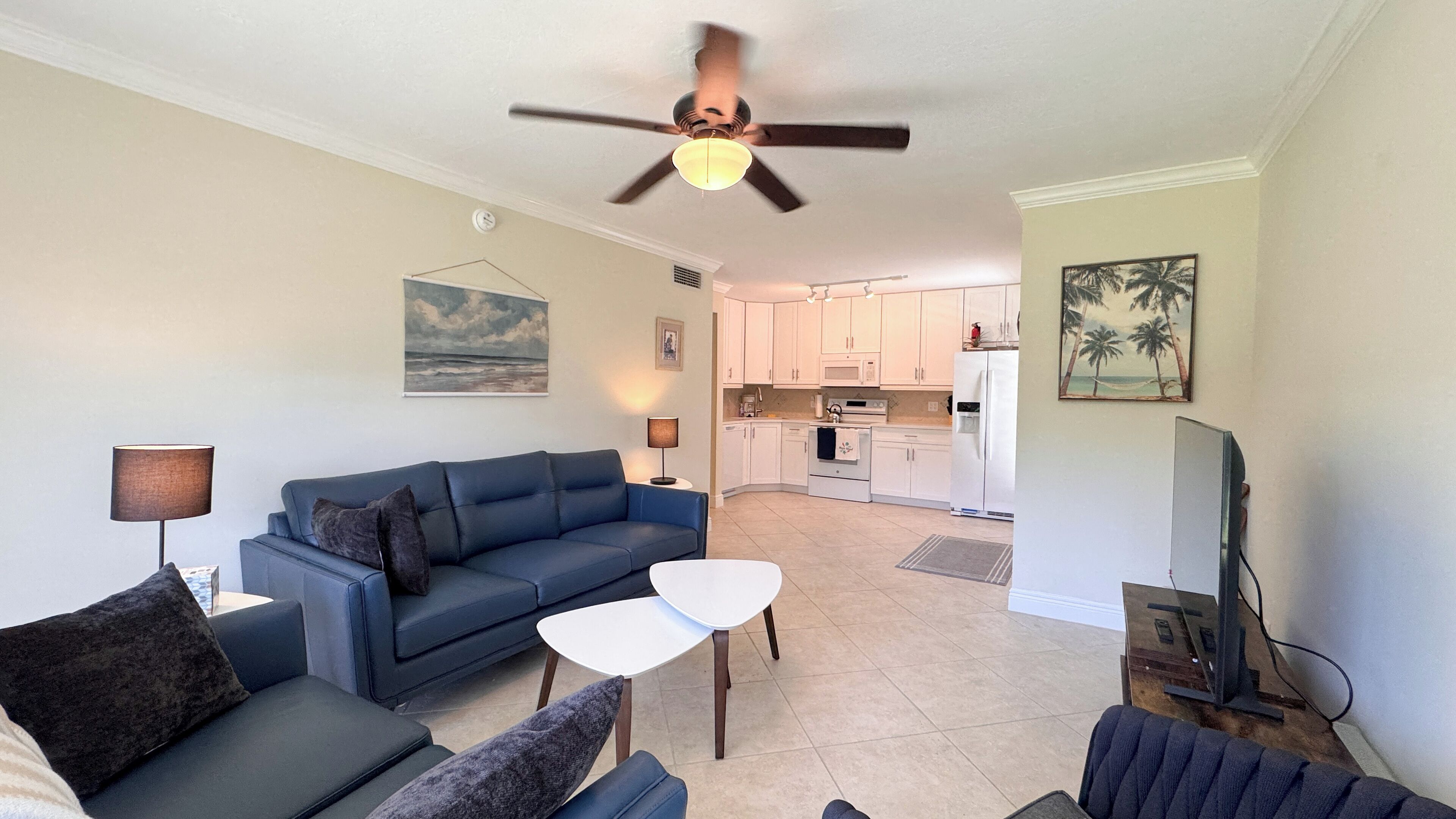 A living room with a blue sofa, a small white table, and a ceiling fan.