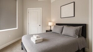 Une chambre à coucher avec un lit, une table de chevet, une lampe, une porte et un tableau encadré au mur.