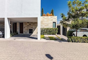 Un bĂątiment moderne dotĂ© dâune entrĂ©e couverte, dâune allĂ©e pavĂ©e et dâune voiture garĂ©e dans lâallĂ©e.