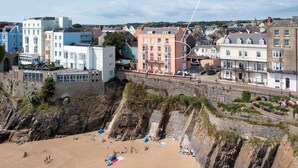 A coastal town with buildings along the cliffside, including a notable pink building labeled '5 Paragon Court, Tenby'. - 5 Paragon Court - Sea Front Apartment (Tenby)