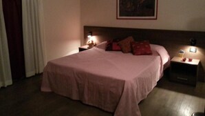 Un dormitori amb un llit gran, dues taules de nit amb làmpades, un quadre a la paret i una finestra amb cortines.