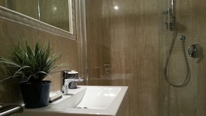 Un bany amb un lavabo blanc, una planta en test i una dutxera.