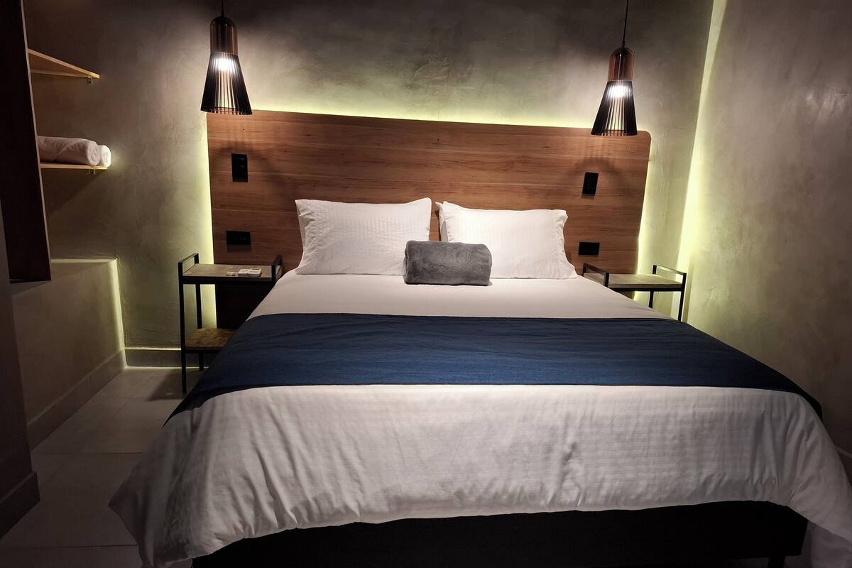 A neatly made bed with a wooden headboard, two bedside tables, and two pendant lights.