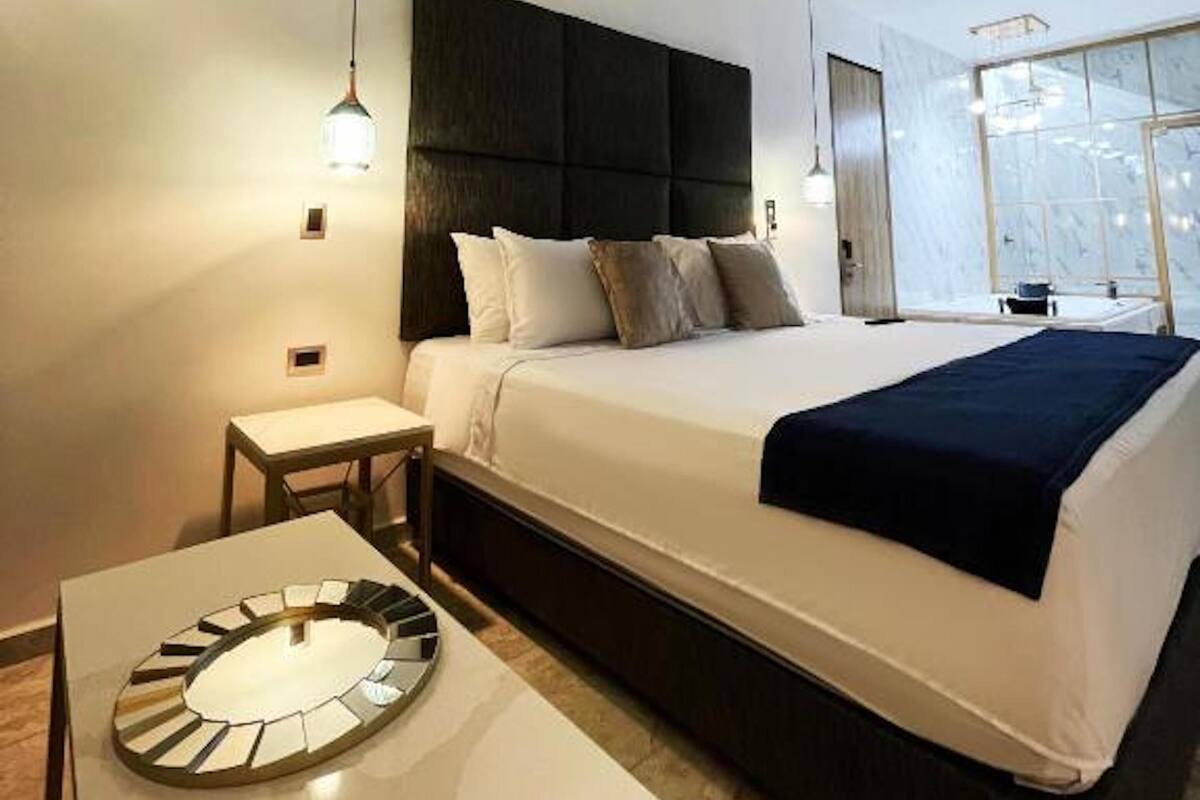 A modern hotel room with a large bed, bedside tables, and a view of the city through a large window.