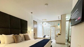 A modern hotel room with a large bed, a flat-screen TV, and a glass door leading to a bathroom. - Hotel Lleras Park II (Medellín)