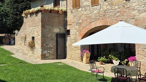 Un bâtiment en pierre avec un toit en tuiles, une cheminée et un patio couvert doté de sièges extérieurs.