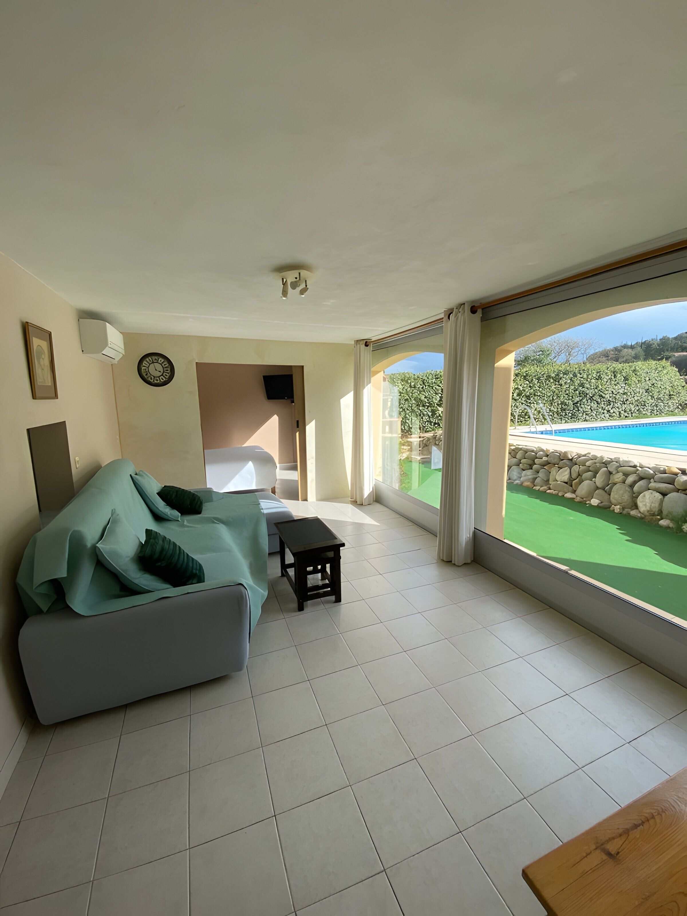 Habitació amb sofà, taula petita, televisió i vista a una piscina.
