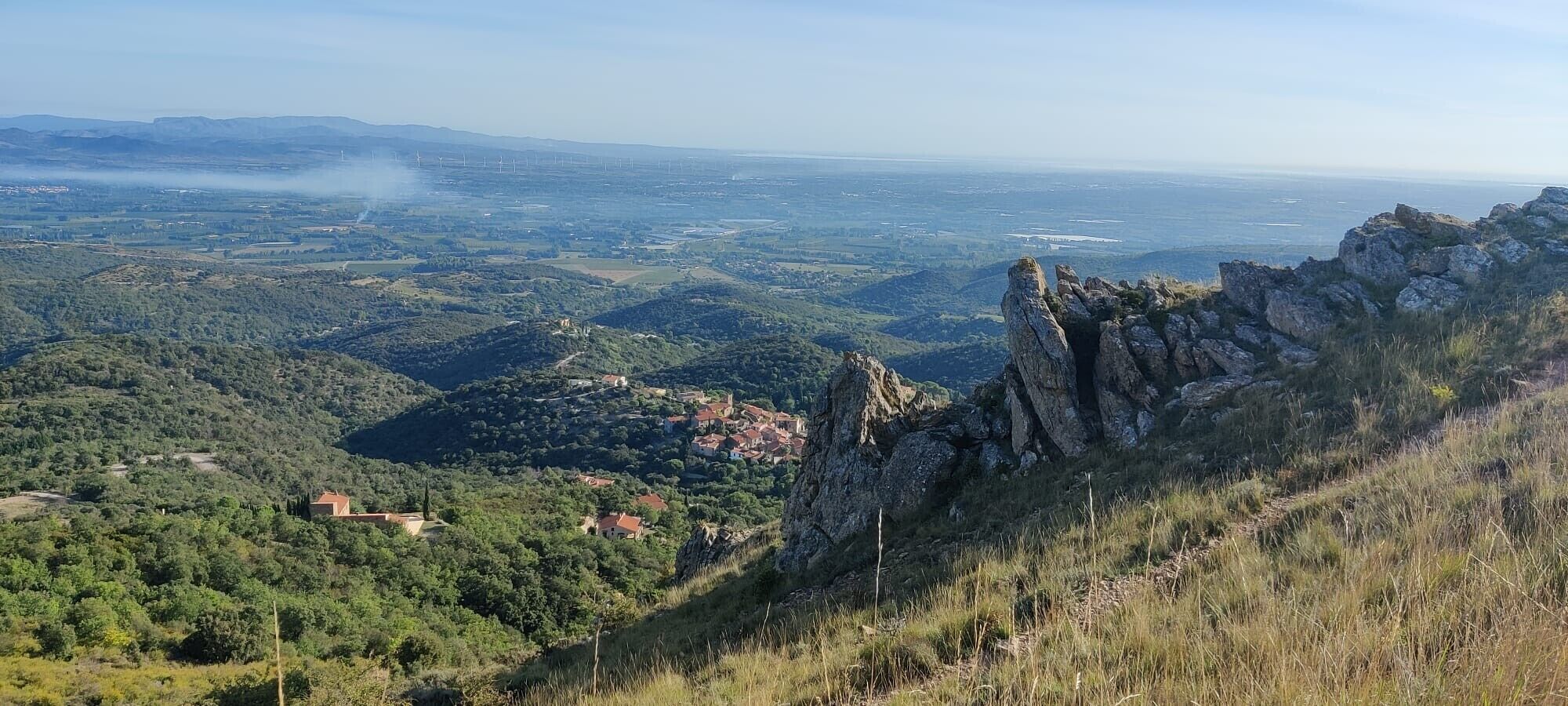A mountainous landscape with a village, rocky outcrops, and distant wind turbines.
