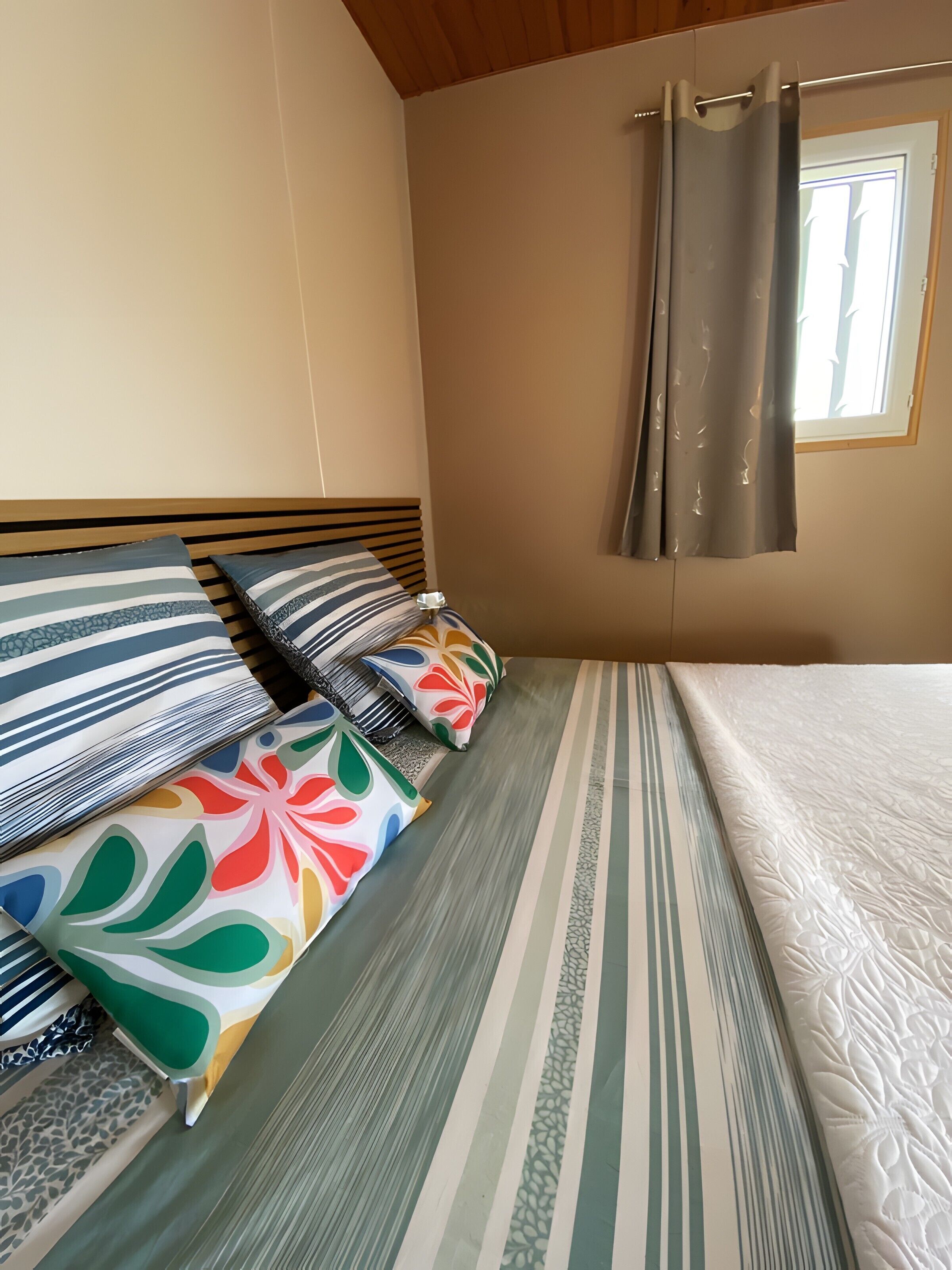 Ein Bett mit gestreifter Bettwäsche, einem Kopfteil und Kissen mit verschiedenen Mustern.