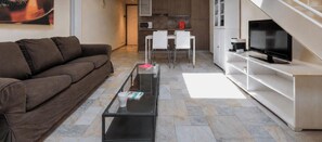 Ein modernes Wohnzimmer mit Sofa, Couchtisch, Fernseher und einer Küchenzeile im Hintergrund.