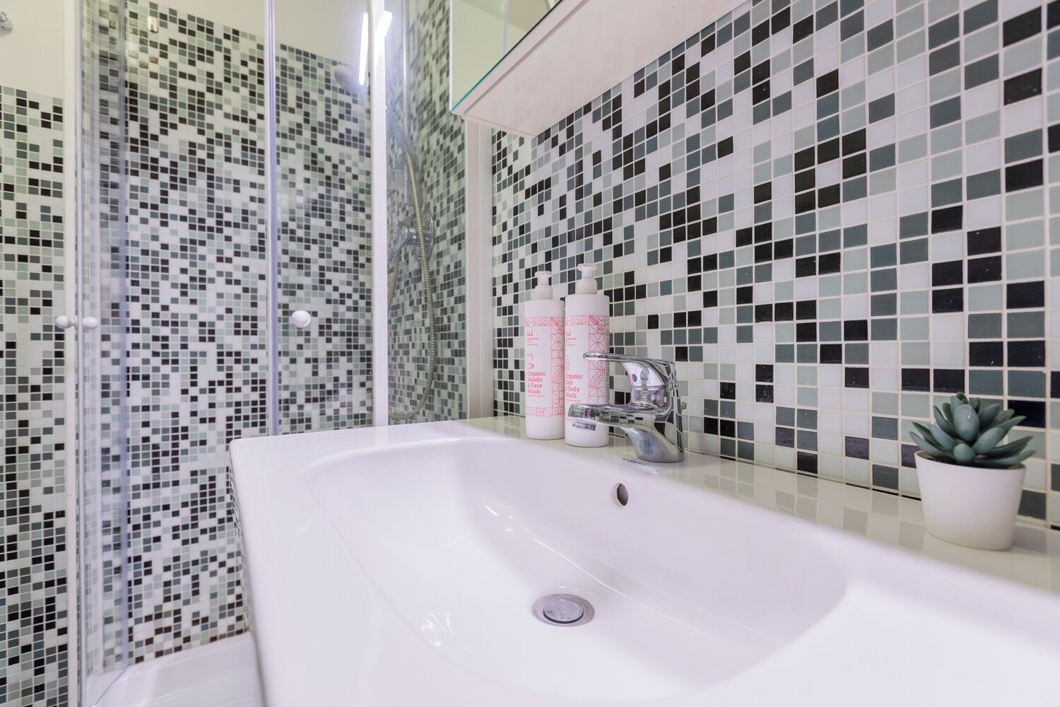 A bathroom with a white sink, a glass shower enclosure, and a tiled wall with a mosaic pattern.