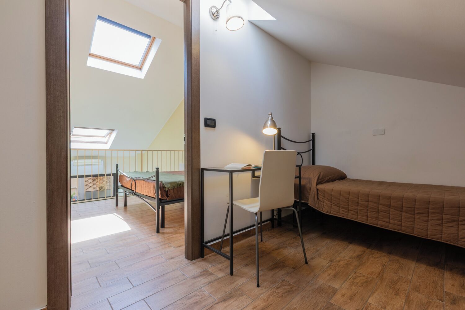 A small, well-lit room with a bed, a desk with a chair, and a skylight.
