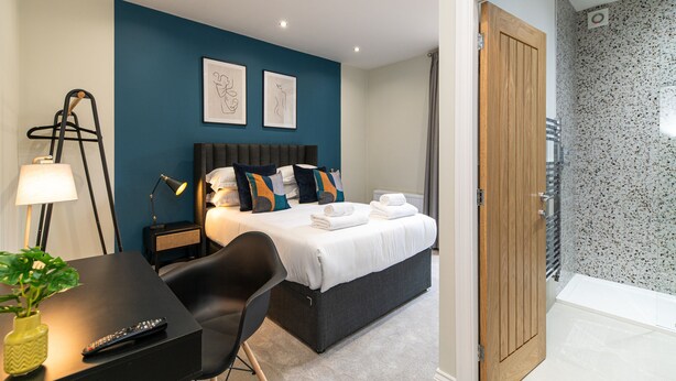 A hotel room with a bed, bedside table, lamp, chair, and a view of the bathroom. - Chelmsford Loft 8 in Newcastle Upon Tyne (Newcastle-upon-Tyne)