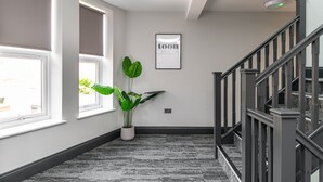 A hallway with a staircase, a potted plant, and a framed sign on the wall. - Chelmsford Loft 8 in Newcastle Upon Tyne (Newcastle-upon-Tyne)