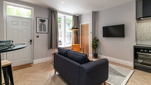 A modern living room with a sofa, a dining table, and a kitchen area with a TV and oven. - Chelmsford Loft 8 in Newcastle Upon Tyne (Newcastle-upon-Tyne)