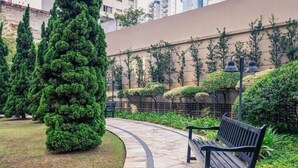 A curved stone pathway leading to a bench in a landscaped garden area with neatly trimmed hedges and trees. - Pinheiros Luxury Flat in a 4-star hotel (São Paulo)