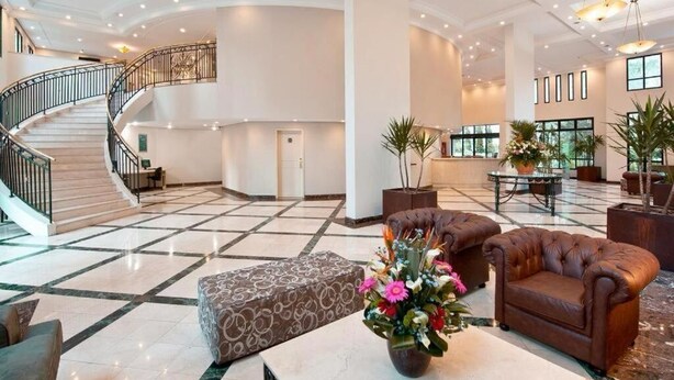 A spacious lobby with a marble floor, a grand staircase, leather sofas, and a central floral arrangement. - Pinheiros Luxury Flat in a 4-star hotel (São Paulo)