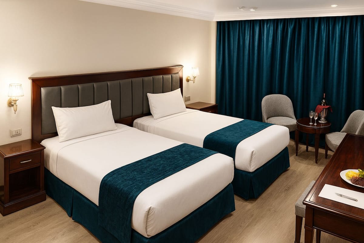 A hotel room with two beds, a desk, a chair, and a table with a bottle and glasses.