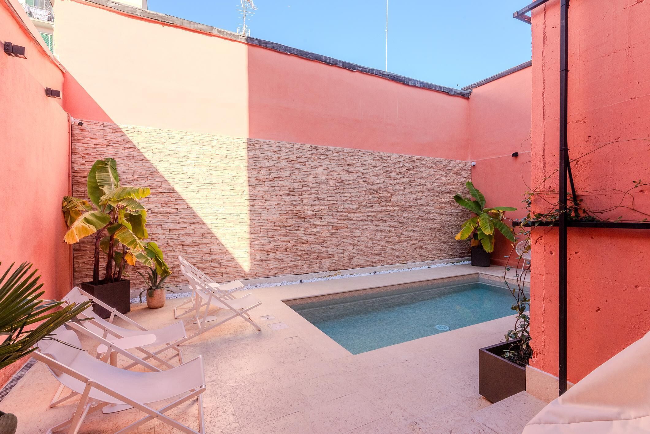 A small outdoor pool area with white lounge chairs and potted plants.