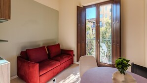Ein Zimmer mit einem roten Sofa, einem Esstisch mit einer Vase und einem großen Fenster mit Blick auf Gebäude und Grünflächen.