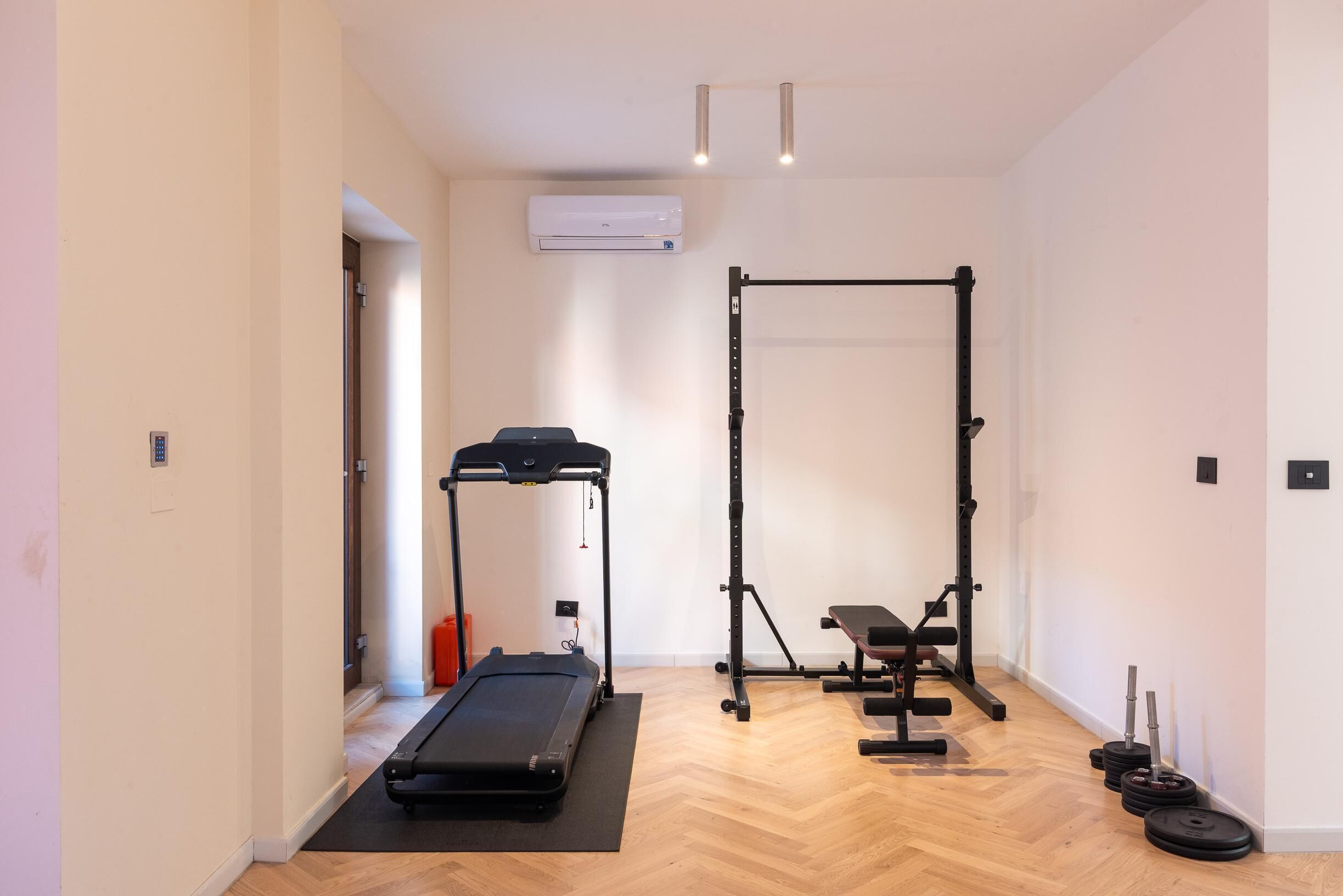 Ein Fitnessstudio mit Laufband, Squat-Rack, Hantelbank und Gewichte.