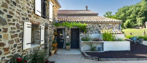 A stone building with a tiled roof, a gravel driveway, and potted plants.