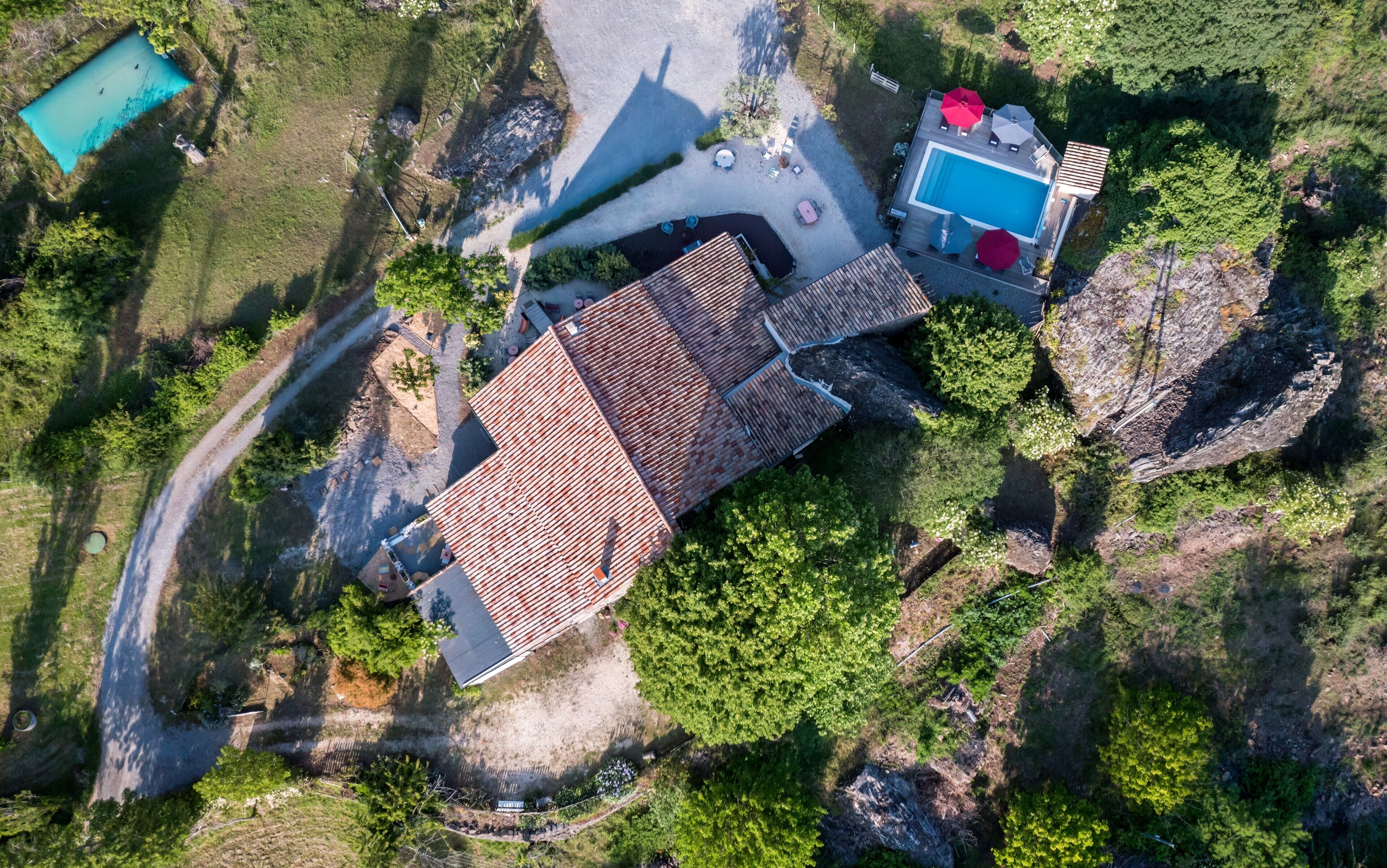 Vue aérienne d’une propriété dotée d’une piscine, d’un espace patio et d’un bâtiment surmonté d’un toit en tuiles.