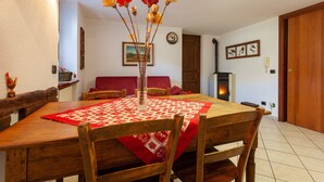 A dining area with a wooden table, chairs, a vase with flowers, a red tablecloth, a fireplace, and a clock on the wall. - A Stone's Throw from Aosta (Pollein)