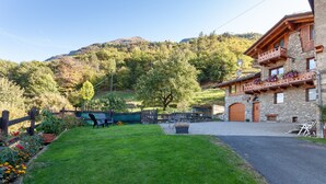 A stone building with a balcony, a paved driveway, and a grassy yard with a wooden fence. - A Stone's Throw from Aosta (Pollein)