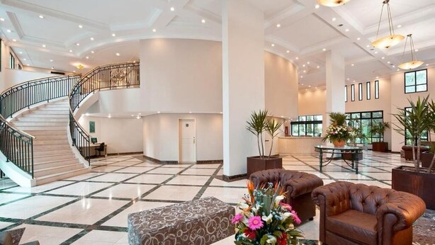A spacious lobby with a marble floor, a curved staircase, and a seating area with a brown leather sofa and ottoman. - Maria Flat in Pinheiros equipped in a 4-star hotel - 4 (São Paulo)