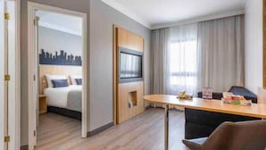 A modern hotel room with a bed, a desk, a chair, a TV, and a cityscape view. - Maria Flat in Pinheiros equipped in a 4-star hotel - 4 (São Paulo)