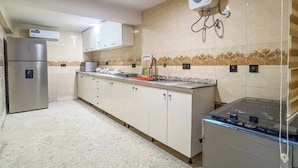 A kitchen with white cabinets, a stainless steel refrigerator, a microwave, and a water dispenser on the wall. - Kpees Apartment (Abuja)