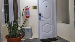 A hallway with a white door marked with the number 114, a fire extinguisher, a potted plant, and a ceiling light fixture. - Kpees Apartment (Abuja)