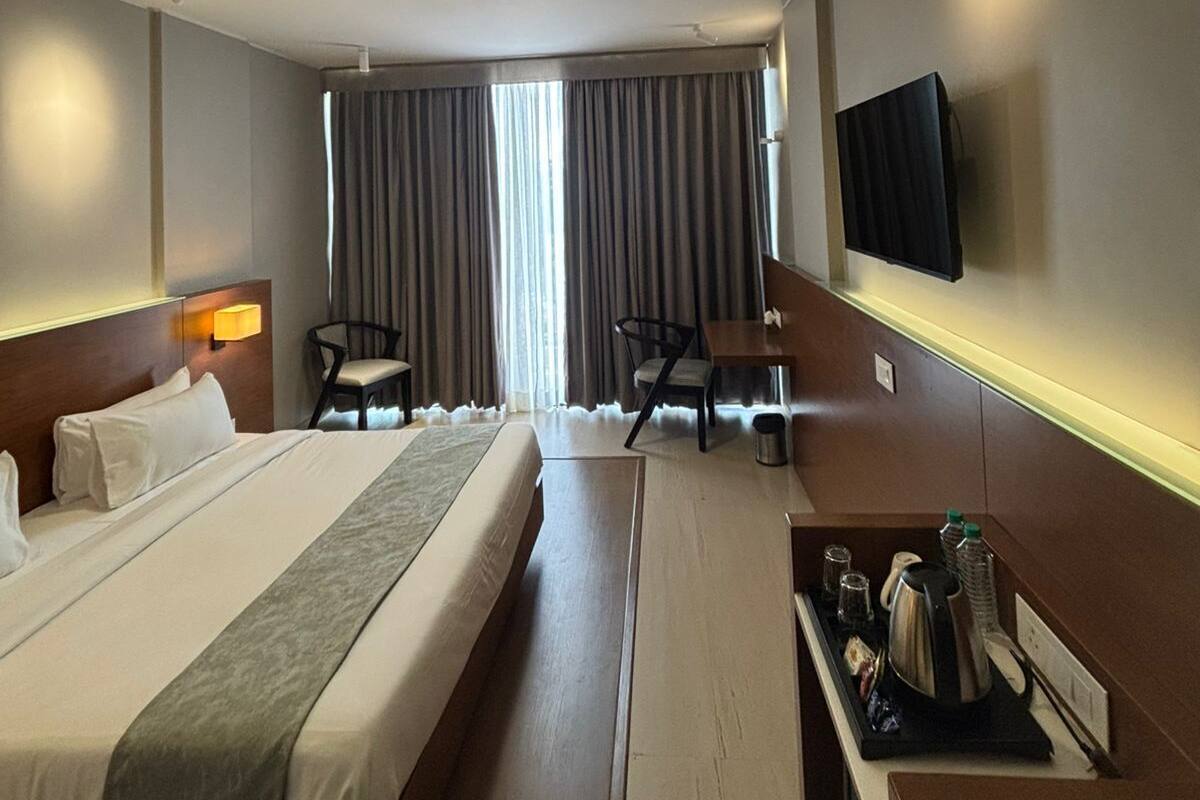Une chambre d’hôtel avec un grand lit, un bureau, une chaise, une télévision et une fenêtre avec des rideaux.