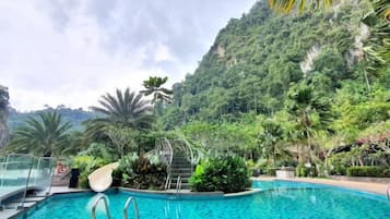 A swimming pool with a clear blue water, surrounded by lush greenery and a mountainous backdrop.