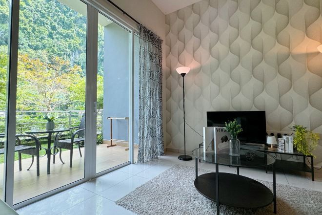 Ein modernes Wohnzimmer mit einer großen Schiebeglasdoor, die auf einen Balkon führt, einem Flachbildfernseher, einem Glastisch und einer Wand mit Muster.