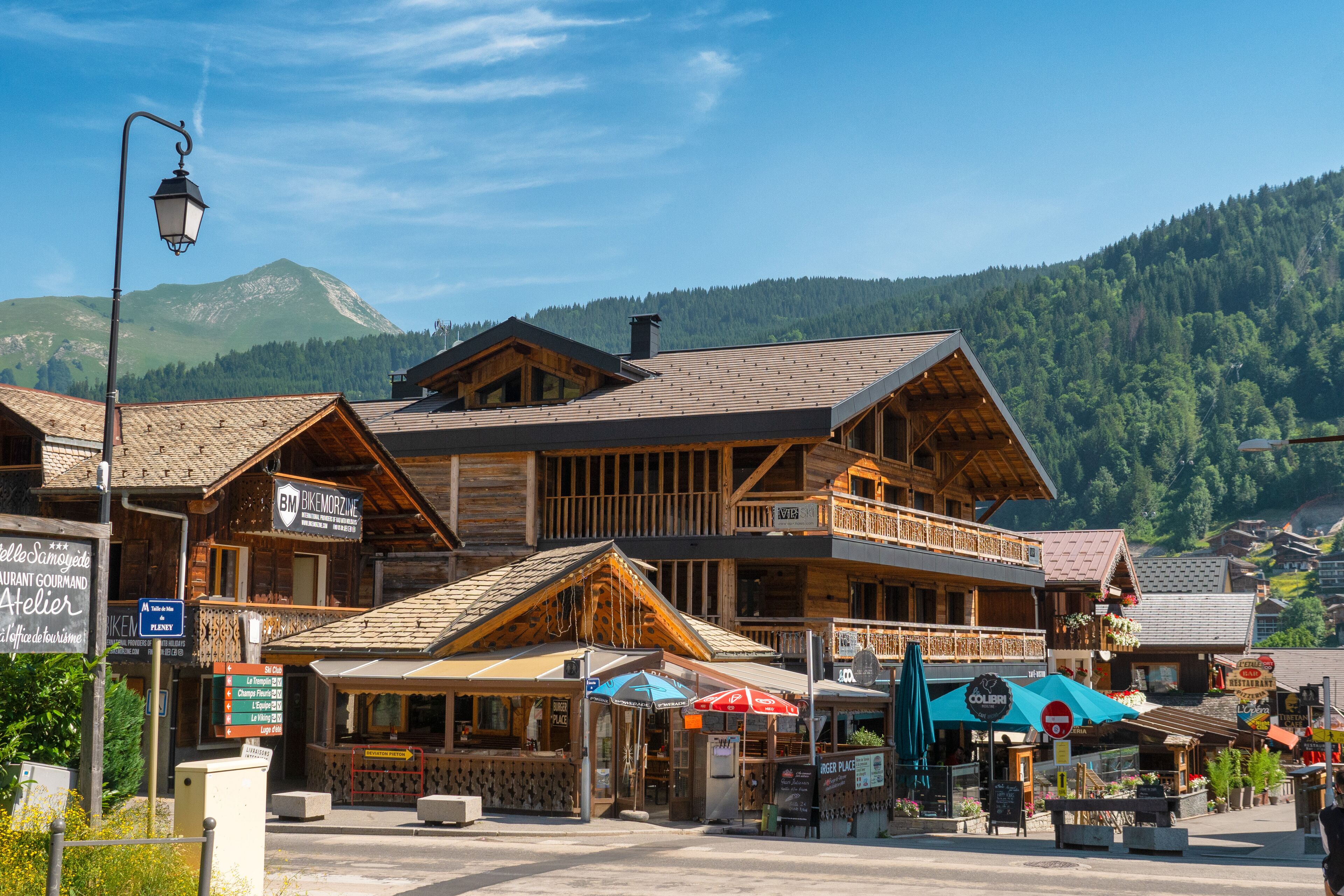 A wooden building with balconies, a sign for 'BKMORZINE', and outdoor seating with umbrellas.