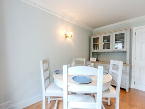 Een eetgedeelte met een ronde tafel en witte stoelen, een keuken met kasten en een wandlamp.
