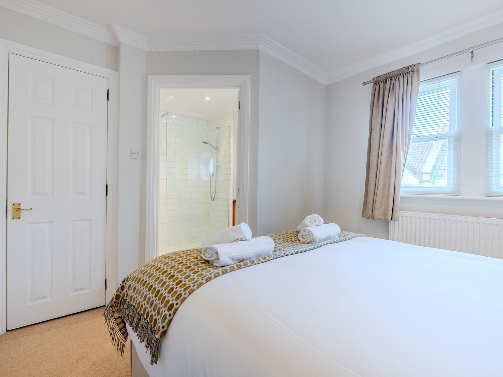 A hotel room with a large bed, a shower area, and a window with curtains.