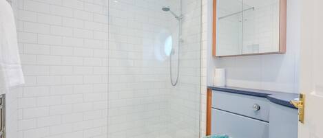 A modern bathroom with white tiled walls, a glass shower enclosure, a toilet with a decorative blue lid, and a vanity with a mirror and a towel hanging on the wall.