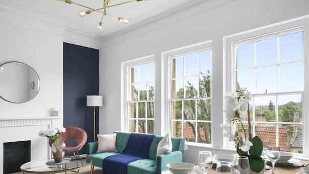 Un salon moderne avec un canapé de couleur turquoise, une table basse ronde et un coin repas préparé pour un repas.