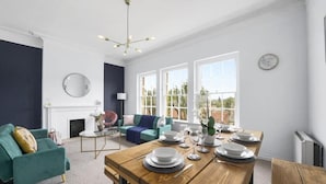 Un salon moderne avec une table à manger en bois pouvant accueillir six personnes, un canapé de couleur turquoise, une cheminée et de grandes fenêtres donnant sur l’extérieur.