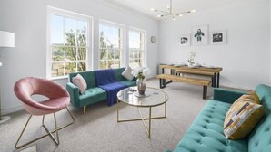 Un salon moderne avec un canapé vert, un fauteuil rose, une table basse en verre et un coin repas comprenant un banc et une table.