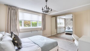 A bedroom with a bed, a desk, a chair, a radiator, a window with curtains, and a mirror reflecting the room. - Spacious Surrey Family Home with Free Parking - Pass the Keys (Addlestone)