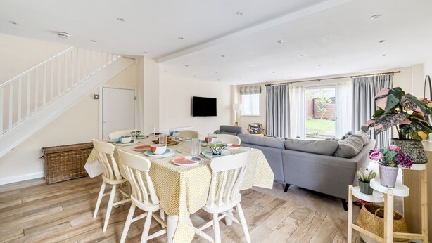 A spacious living area with a dining table set for four, a grey sofa, and a staircase leading to another room. - Spacious Surrey Family Home with Free Parking - Pass the Keys (Addlestone)