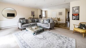 A modern living room with a grey sectional sofa, a coffee table, and a large round mirror on the wall. - Spacious Surrey Family Home with Free Parking - Pass the Keys (Addlestone)