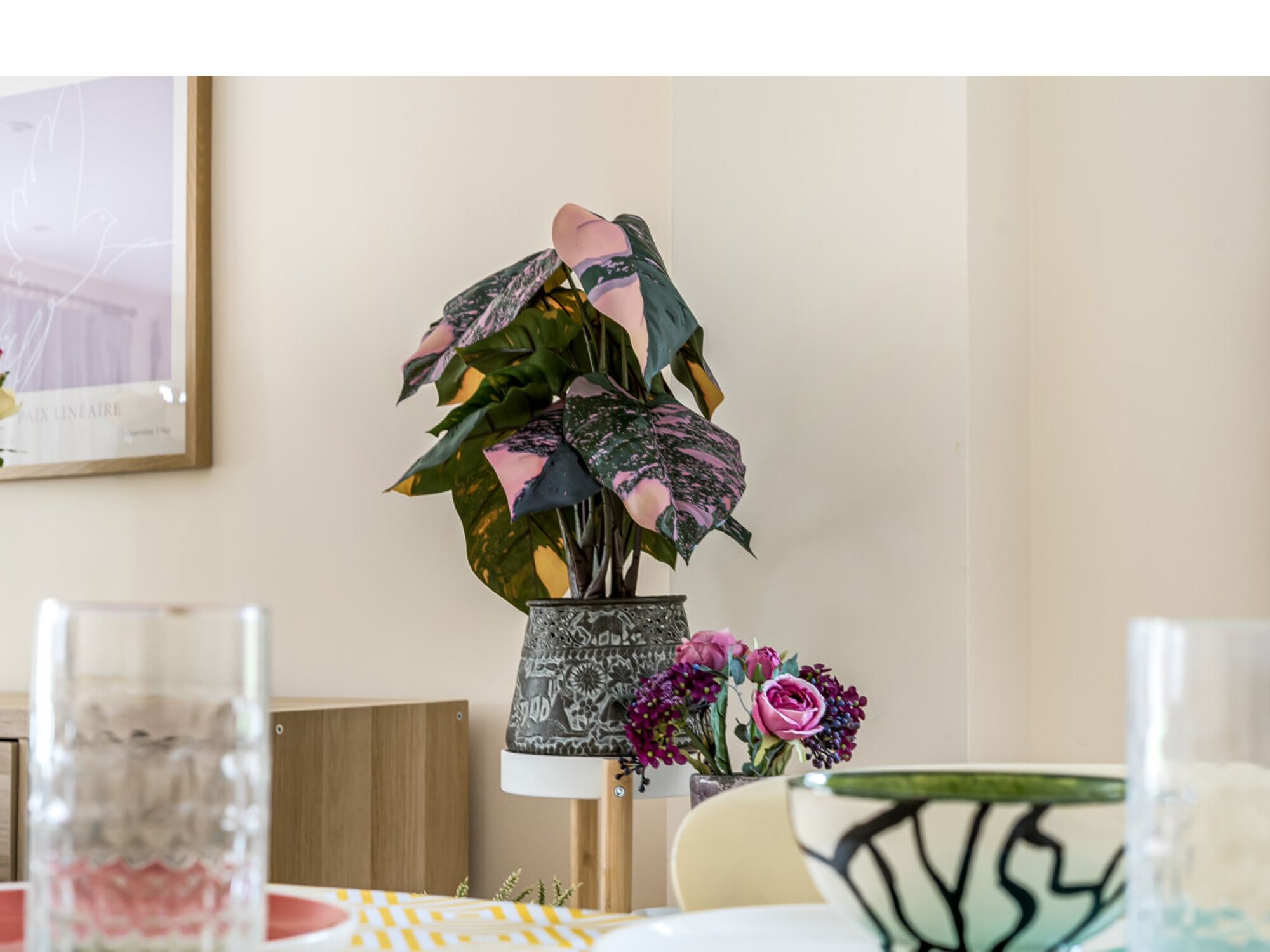 A dining table with a vase of flowers, a framed picture on the wall, and a glass of water.