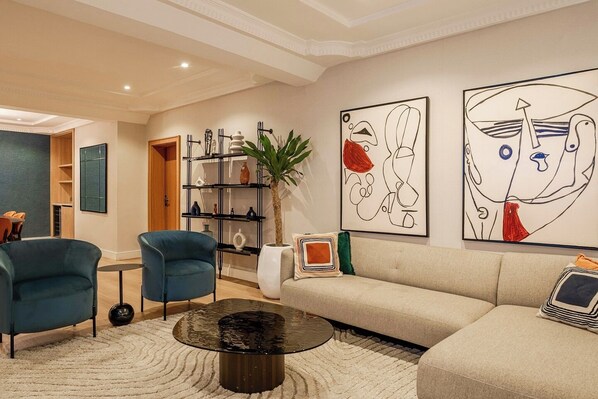 A modern living room with a sofa, two armchairs, a coffee table, and abstract wall art.